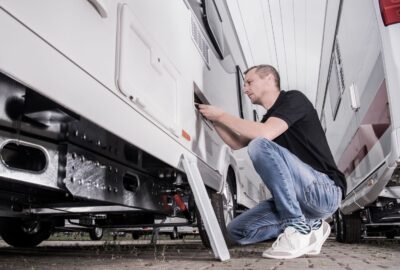 A man kneeling and working on an exterior compartment of a white RV.