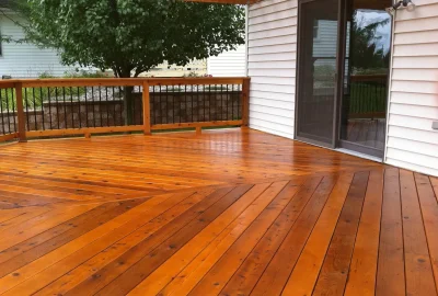Newly stained wooden deck with herringbone pattern boards, wood railing, and sliding glass door.