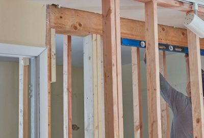 A person uses a blue level to check the alignment of wooden wall studs during a home renovation.
