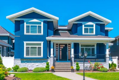 Bold blue two-story home with white trim, stone base, manicured green lawn, and a paved walkway.