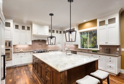 Spacious kitchen with white cabinets, a dark wood island with marbled countertop, and black lantern pendant lights.