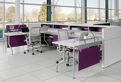 Modern open-plan office cubicles with white desks, purple accents, and mesh ergonomic chairs near large windows.