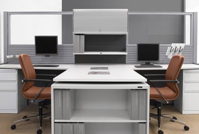 Modern office workstation with two side-by-side desks, computer monitors, and brown ergonomic chairs.