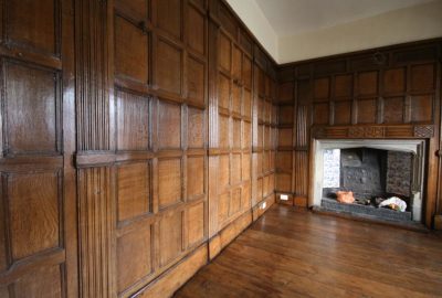 A room with dark wood paneling, a wooden floor, and a stone fireplace decorated with blue and white tiles.