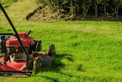 Person pushing a red lawn mower across a bright green lawn.