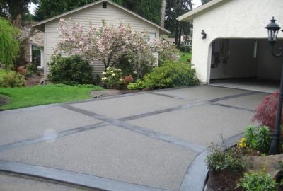 Decorative grey concrete driveway with a dark grid pattern, leading to a white house and garage.
