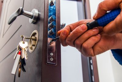 Hands using a tool to adjust the locking mechanism of a brown door with keys in the lock.