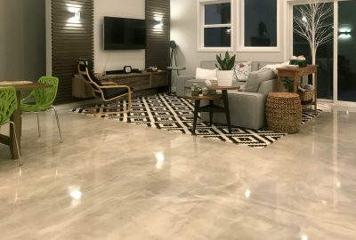 Modern living room with polished concrete floors, a gray sofa on a geometric rug, and bright green dining chairs.