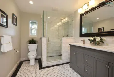 Modern bathroom featuring a glass walk-in shower, grey vanity with marble countertop, and white mosaic flooring.