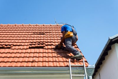 A roofer using a power drill to repair a red tile roof.