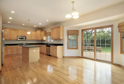 Modern kitchen with light wood cabinets, black countertops, an island, and sliding glass doors leading to a wooden deck.