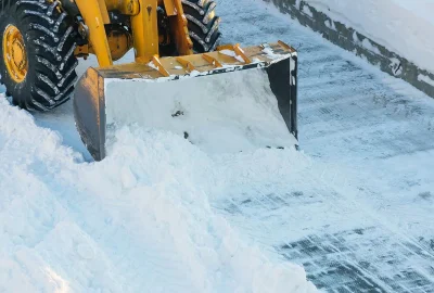 A yellow front-loader pushes a pile of snow along a snowy road.