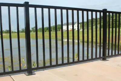 Black metal picket fence overlooking a pond and a white farmhouse in the distance.