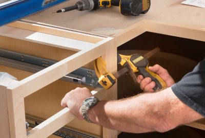 Person assembling wooden cabinetry using a bar clamp and drawer slides on a workbench.
