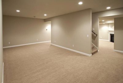Empty finished basement with beige walls, tan carpeting, and recessed ceiling lights.