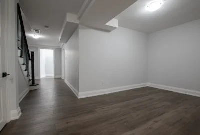 Empty room with light gray walls, dark wood flooring, and a staircase with a black railing.