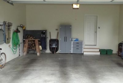 An empty, organized garage with tools, a grey storage cabinet, a wheelbarrow, and a white door at the back.