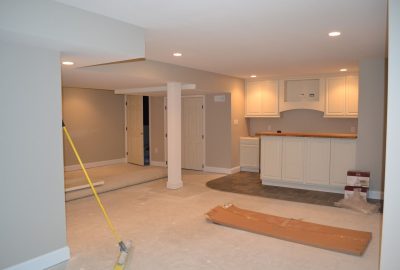 Basement renovation with white cabinetry, recessed lighting, and unfinished floors with construction materials.