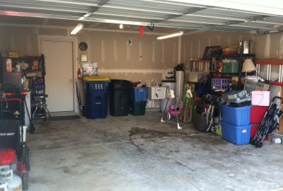 A cluttered garage interior filled with storage bins, strollers, and miscellaneous household items.