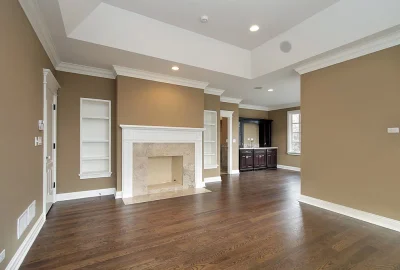 Living room with dark wood floors, tan walls, white fireplace mantle, built-in shelving, and a wet bar in the background.