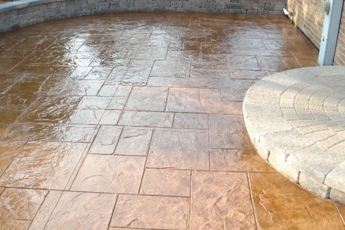 Glossy brown stamped concrete patio with a grey stone retaining wall and circular stone pavers.