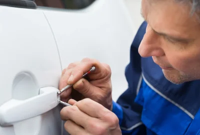 Locksmith in blue overalls picking the lock of a white car door.