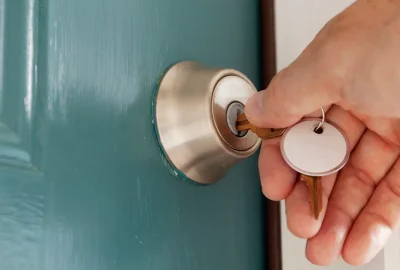 Hand inserting a key into a silver lock on a teal door.