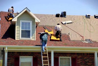 Three roofers working on a house roof replacement under a clear blue sky.