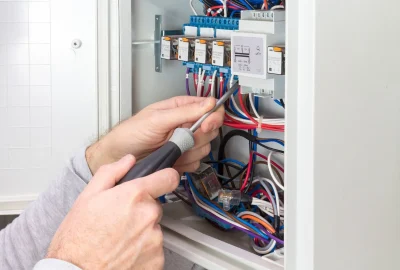 *   Image content: A person's hands using a screwdriver to work on an electrical panel.
    *   Details: The panel contains v