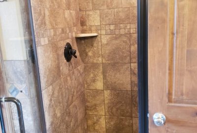 Walk-in shower with tan tiled walls and floor and dark bronze fixtures.