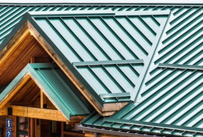 Close-up view of a multi-gabled teal metal roof over a wooden building with natural wood eaves.
