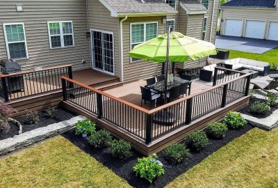 Multi-level wooden deck with a dining set and green umbrella, overlooking a landscaped patio and garden.