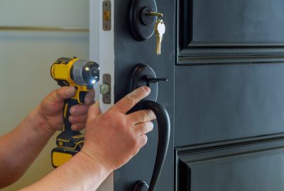 Hands using a yellow power drill to install a lock on a black door.