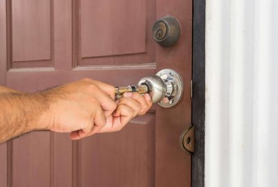 Hands pulling a silver doorknob off a brown door.