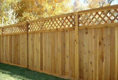 Wooden privacy fence with a lattice top, set against a backdrop of yellow autumn trees.