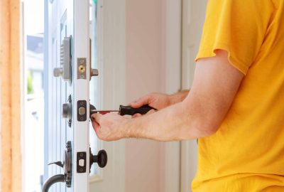 Person in a yellow shirt using a screwdriver to install or repair a door lock.