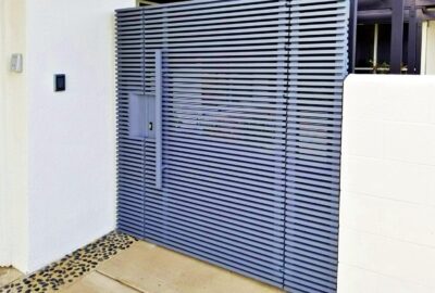 Modern grey horizontal slatted gate between a white wall with a keypad and a white masonry wall.