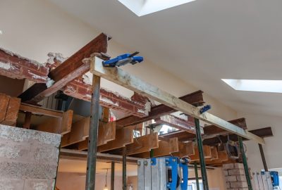 Construction site showing steel beams and wooden supports propped up by metal telescopic floor props.