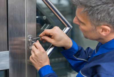 Locksmith in a blue uniform picking a lock on a stainless steel door.