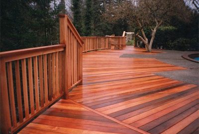 Polished reddish-brown wooden deck with railings, surrounded by evergreen trees.