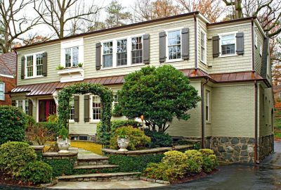 Sage green two-story home with grey shutters, copper roof accents, and a landscaped garden with a stone walkway.