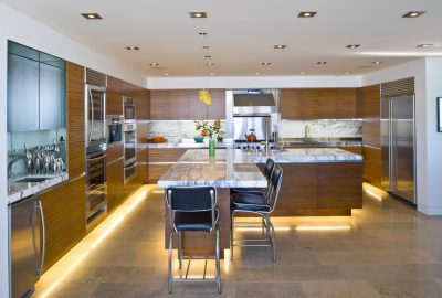 Modern kitchen with wood cabinetry, marble countertops, stainless steel appliances, and a large island with black stools.