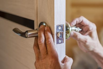 Hands installing a silver lever handle and lock mechanism on a light-colored wooden door.