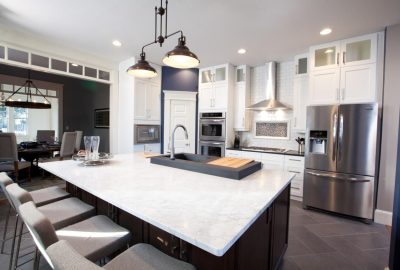 Modern kitchen with a white marble island, dark cabinets, stainless steel appliances, and gray bar stools.