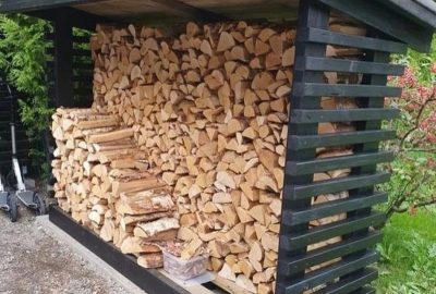 Black wooden log store filled with stacked split firewood.
