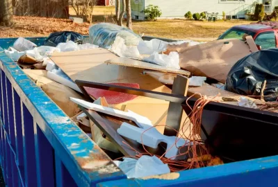 Blue dumpster filled with cardboard, wood, and plastic waste in a residential neighborhood.