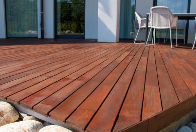 Polished reddish-brown wooden deck next to a modern white house with white patio furniture.