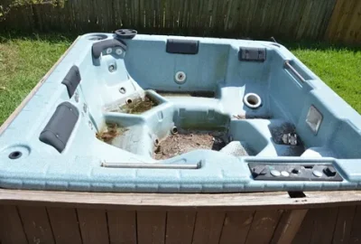 An empty, light blue hot tub with dark headrests sits in a wooden frame on a grassy lawn.