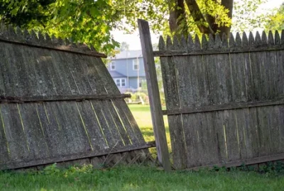 A weathered wooden picket fence with a section leaning heavily to the left, creating a large gap.