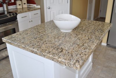 Kitchen island with a tan speckled granite countertop and a white bowl on top.